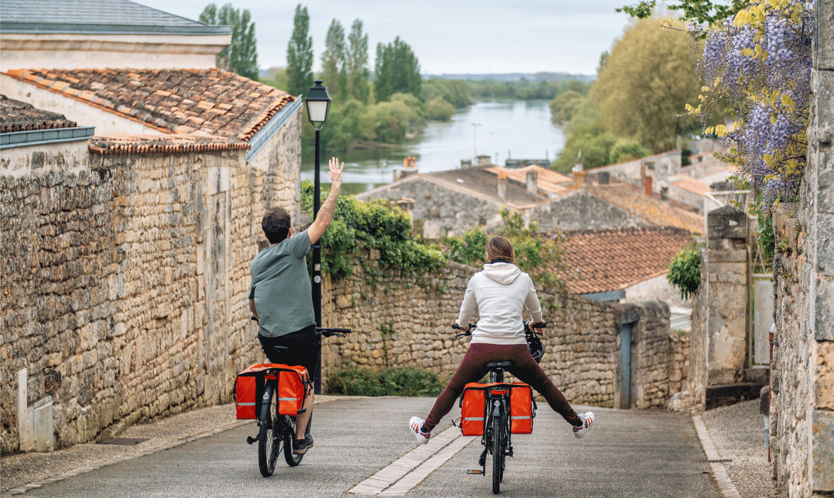 2 cyclistes dans une rue bordée de murs en vielles pierres avec la charente en ligne de mire